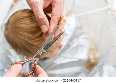 Man's Hands Doing Blonde Toddler Haircut With Hairdresser Scissors At Home. Baby Boy Hair Cut Diy