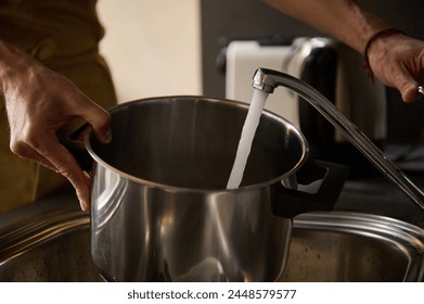Man's hands filling a stainless steel saucepan with running water until it boils and cooks something. The concept of preparing food in the home kitchen. Close-up