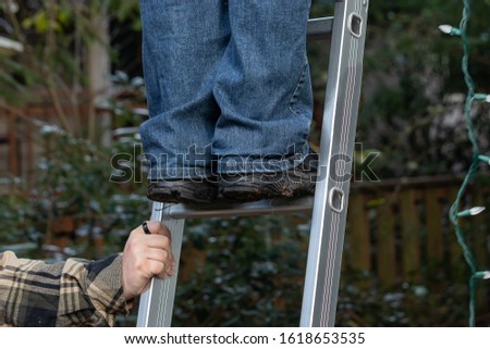 mans hands hold a silver ladder steady so another man can climb