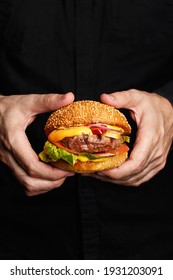 Man's hands holding beef burger. Close up, side view, copy space. Junk food, fast food