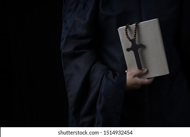 Man's Hands Holding Bible And Rosary During Prayer - On Black Background