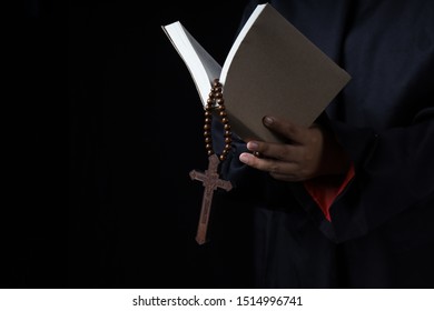 Man's Hands Holding Bible And Rosary During Prayer - On Black Background