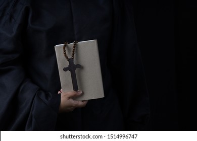 Man's Hands Holding Bible And Rosary During Prayer - On Black Background