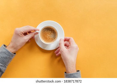 Man's Hands Holding A Cup Of Coffee On Yellow Table, Top View