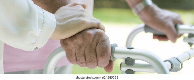 Man's hands holding the walking frame with carer support - Shutterstock ID 624585353