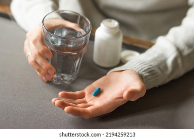 Man's hands holds a blue capsule and glass of water over the table, ready to take medicines. Sick man need medicine from headache and cold, painkiller, nutritional supplement. Health care concept.  - Shutterstock ID 2194259213