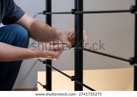 Man's hands installing components of a modern black metal balustrade with a screwdriver