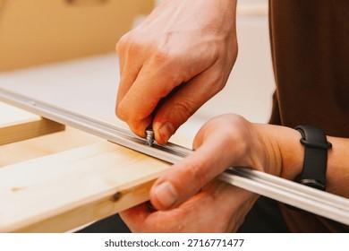 A man's hands manually screw in a screw, assembling the base of a bed in a room.