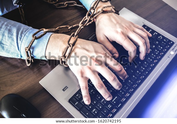 Man\'s hands in old rusty chains.\
In the trap of office work. Routine job. Manager near the\
laptop.