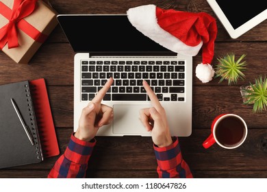 Man's hands on laptop, showing at screen. Work on Christmas Eve. Top view on human hands, computer keyboard, coffee, Santa hat, gift and digital tablet wooden table background. - Powered by Shutterstock