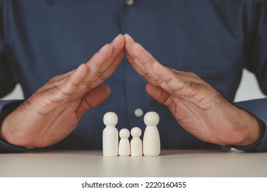 Man's hands protecting wooden figures of family members, Family relationship symbol, family home lockdown concept , Insurance and property investment, world mental health day. Wooden puppets. - Shutterstock ID 2220160455