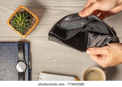 Man's hands show empty black leather wallet with notebook, men's watch, pen and houseplant in a pot on the background