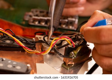 man's hands soldering a electric guitar wire in his workshop