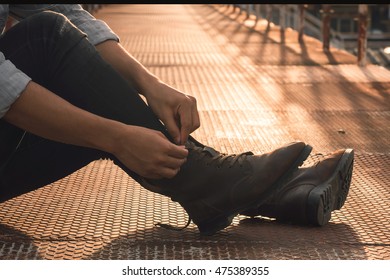 Man's hands tying shoes, Brown leather boots on a bridge at sunset, Men fashion.Toned picture