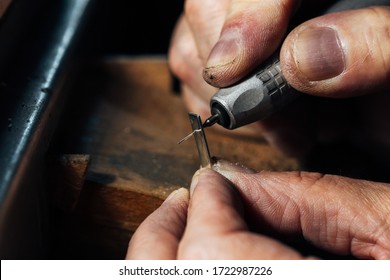 A man's hands work the silver with a drill in a jewelry workshop. The piece of sterling silver is handmade by a goldsmith.