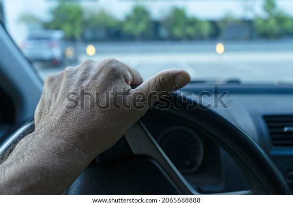 A man\'s left\
hand on the steering wheel of a modern car with a black interior \
Blurred view of the\
background