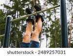 A mans legs in gravity boots hangs on a horizontal bar outdoors on a summer day. 