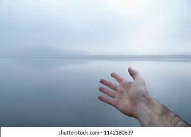 A man's outstretched hand reaching to a open landscape on a misty river. - Powered by Shutterstock