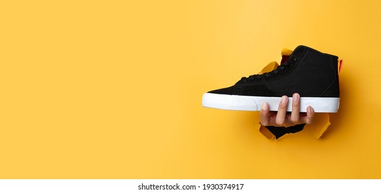 The Man's Right Hand Went Through The Yellow Paper Wall While Holding A Black Shoe. Suitable As A Banner Design Mock Up. Composition Of Photos Using The Rules Of Third. Advertisement