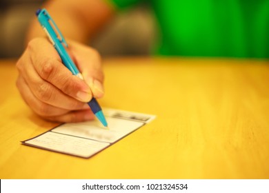 Man's Right Hand Writing On The Lucky Draw Coupon, Memo, Comment, Suggestion Or Questionnaires On The Wooden Table In The Restaurant Or Shop Concept With Copy Space