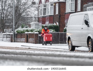 Mansfield Nottingham UK January 12th 2021 Royal Mail British Post Man In Deep Cold Snow Falling On Road And Icy Frozen Pavement Delivering Letters With Trolley Red Uniform During Severe Weather