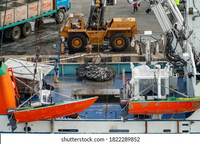 Manta, Ecuador - December 2, 2008: Fishing Vessel Is Unloaded At Dock. Big Net Filled With Tuna Fish Is About To Be Lifted By Crane Off Deck Of Boat. People At Work. Red Speed Boats Up Front.