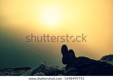 Man-tourist sits on the edge of mountain cliff with his legs dangling over a precipice in colorful mist.