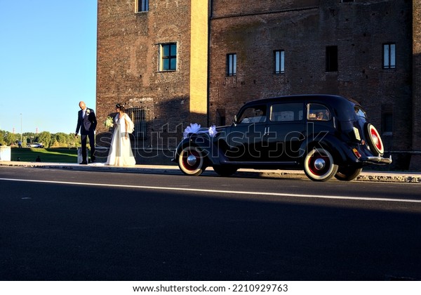 Mantova, Italy - September 2022 - Wedding\
photoshoot next to a historic car at\
sunset