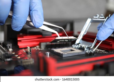 Manual Assembly And Repair Mechanical Device. Hands In Blue Gloves Hold Tongs. Technician Collects Metal Parts And Mounts Them On Device Lying On Table. Small Parts Are Attached With Tweezers.