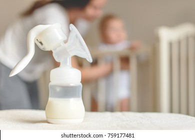 Manual breast pump and bottle with breast milk on the background of mother and baby near the baby's bed.