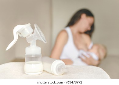 Manual breast pump and bottle with breast milk on the background of mother holding in her hands and breastfeeding baby. Maternity and baby care.