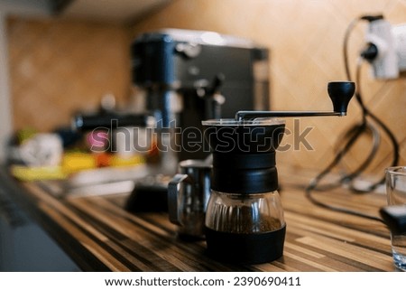 Manual coffee grinder with ground coffee stands on the table near the coffee machine