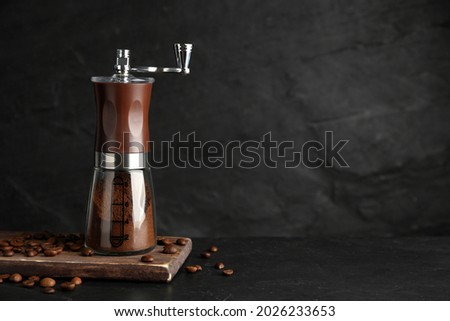 Manual coffee grinder with powder and beans on black table. Space for text