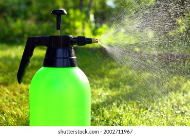 Manual garden sprayer with black handle, spraying smallest drops of water, dust in backlight of evening summer sun against background of green mowed lawn, trees, leaves. Watering and spraying plants - Powered by Shutterstock