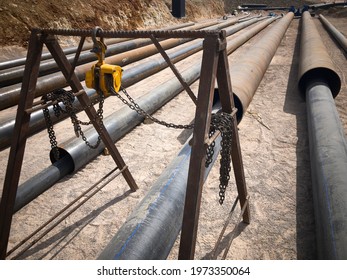 Manual Hoist And PVC Pipes In Protective Metal Covers. Industrial Pipeline Mantling At Construction Site