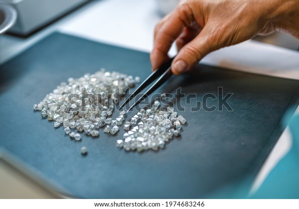 Manual sorting of diamonds. A hand\
with tweezers transfers diamonds from one pile to\
another.
