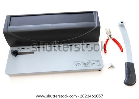 A manual spiral binding machine with a handle, pliers, and a screw is displayed on a white background