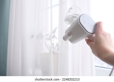 A manual steamer of clothes in hands. Cleaning and maintenance of the interior. - Shutterstock ID 2248202213
