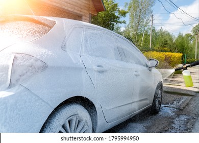 Manual Unknown Car Wash With High Pressure Water Equipment Pump At Home Backyard Outdoors On Bright Shiny Summer Day. Vehicle Covered With Foam Shampoo Chemical Detergents During Carwash Self Service.