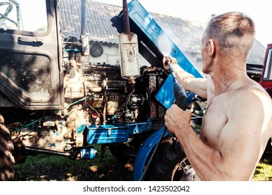 Manual Wash Tractor Engine With Pressure Water. Man Spraying Pressure Washer For Tractor Wash.