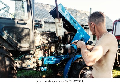 Manual Wash Tractor Engine With Pressure Water. Man Spraying Pressure Washer For Tractor Wash.