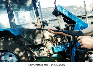 Manual Wash Tractor Engine With Pressure Water. Man Spraying Pressure Washer For Tractor Wash.