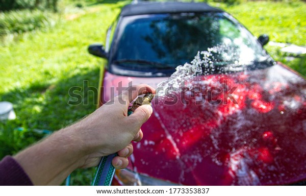 manual washing of a red car in the yard with a\
water hose.