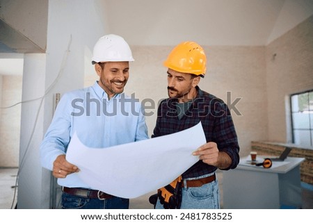 Manual worker and construction site engineer going through hosing plans at renovating home. 