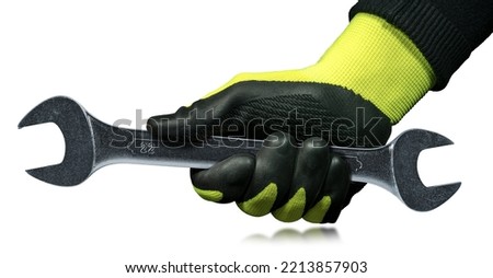 Manual worker with green and black protective work glove holding a stainless steel wrench or spanner, isolated on white background.