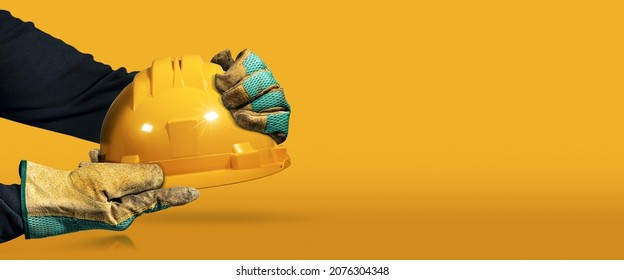 Manual Worker With Protective Work Gloves Holding A Yellow Safety Helmet On A Yellow And Orange Background With Copy Space And Reflections. Concept Of Workplace Security.