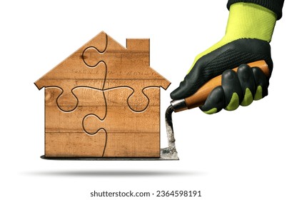 Manual worker with protective work gloves holding a dirty trowel and a small wooden house formed from jigsaw puzzle pieces. Isolated on white background. - Shutterstock ID 2364598191