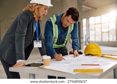 Manual worker and real estate developer analyzing construction plans at building site.  