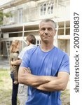 Manual worker standing looking at camera arms crossed young couple standing in background