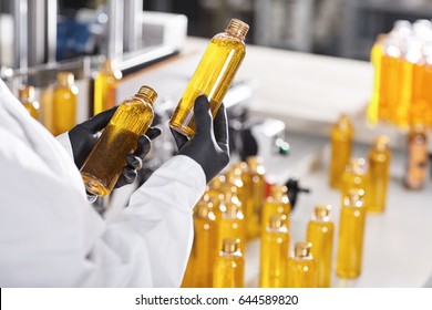 Manufacturing concept. Factory worker holding two glass bottles with yellow liquid comparing quality between them. Factory process of production shampoo. Technology, innovation and scientific concept